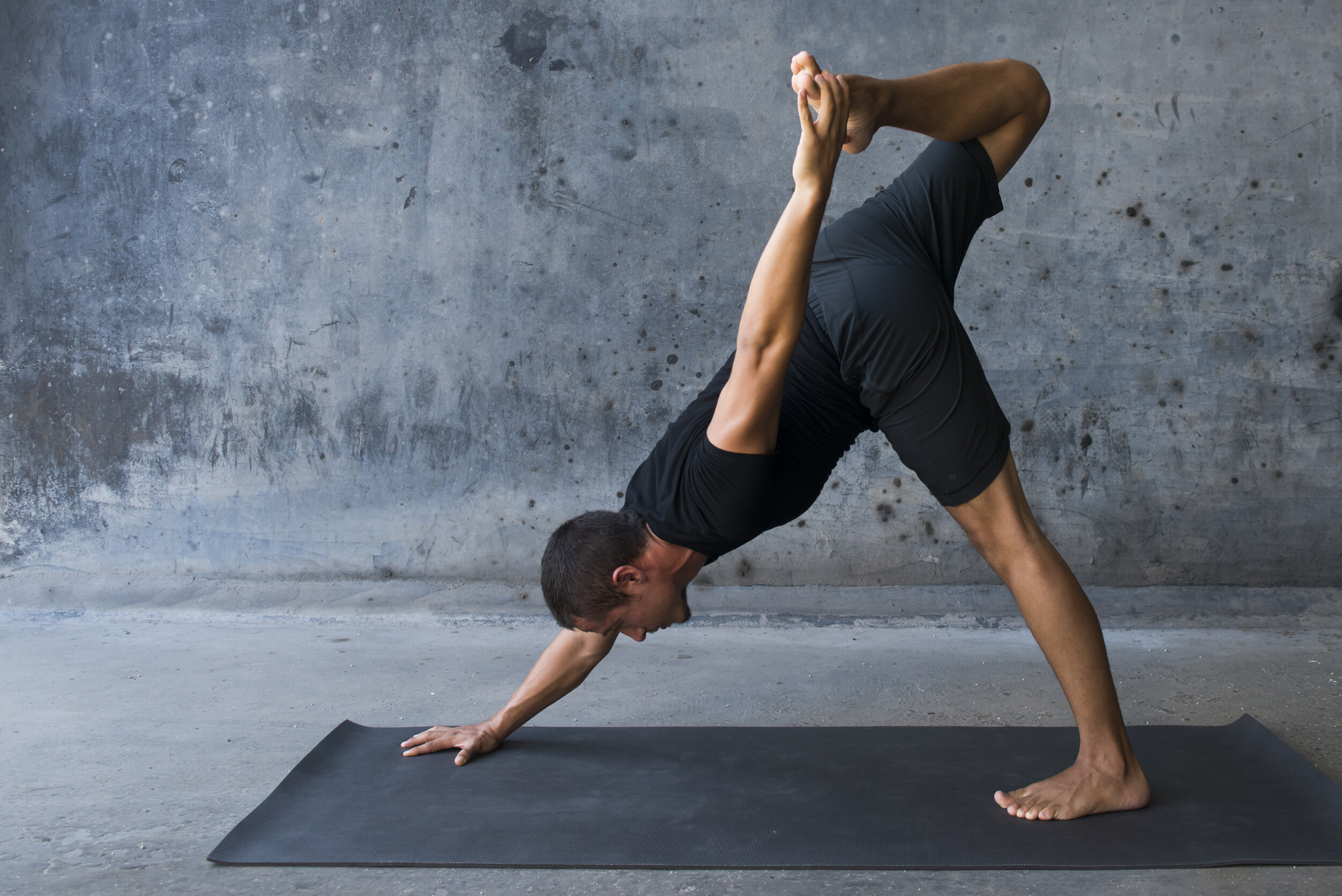 Yoga Praktizierender vor städtischem Hintergrund zeigt eine Variante der Adho Mukha Svanasana